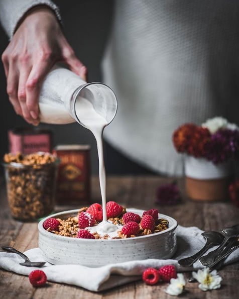Hand pouring milk over granola with raspberries
