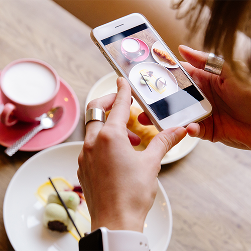 hands holding iPhone taking photo of plate of food and tea below